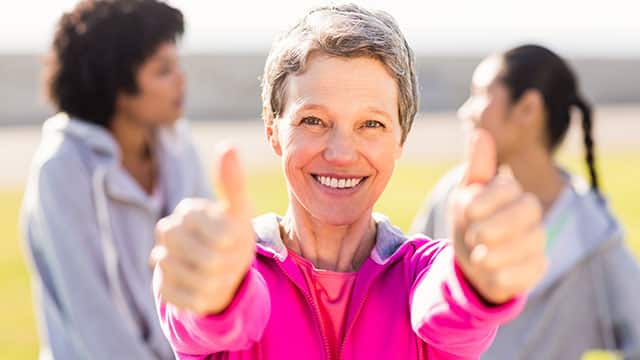 grey-haired woman in pink sweatshirt holding thumbs up