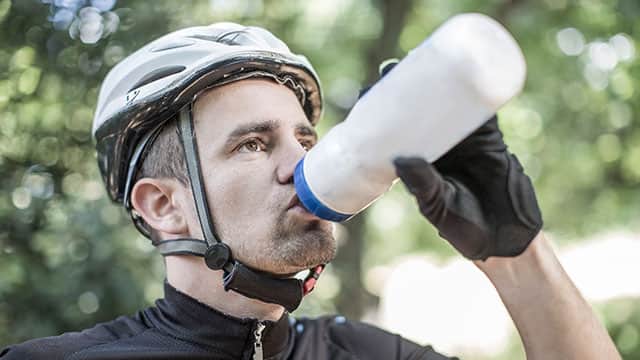 Man in a bicycle helmet taking a break to drink out of a water bottle