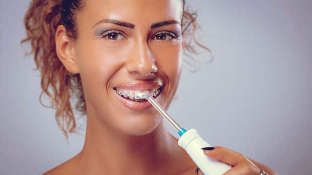 A woman with braces uses a water flosser.