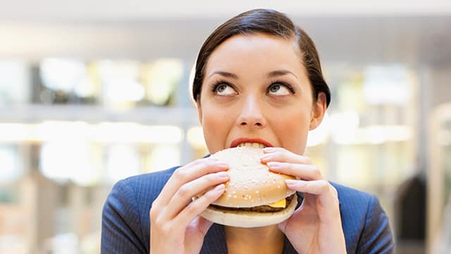 Young woman about to bite on a hamburger, doubtful eyes looking upward like thinking "Is this burger too spicy for my sores?"