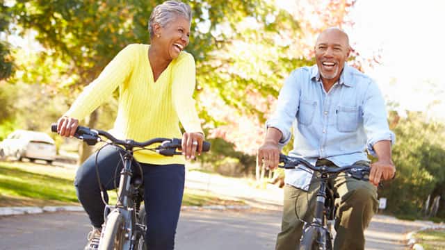 A middle-aged couple riding bikes outside smiling