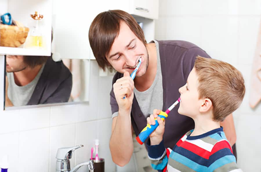 Father and son brushing their teeth in the bathroom in front of the mirror