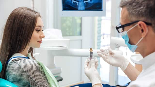 A male dentist shows a female patient how a dental implant looks