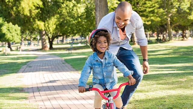 parent helping child ride bike