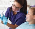 A female dentist in purple scrubs talking with a young female patient