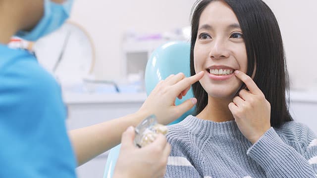 A woman talking to a dentist as they both point to her teeth in the dental clinic