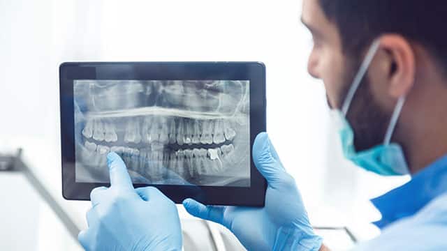 Dentist showing teeth x-ray on tablet and pointing at the screen