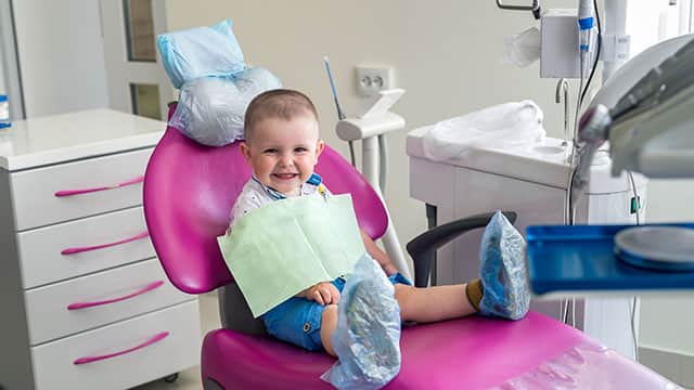 baby smiling while sitting in a dental chair 