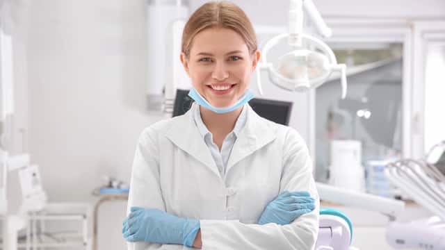 Portrait of a female dentist with arms crossed, smiling, and standing in her clinic
