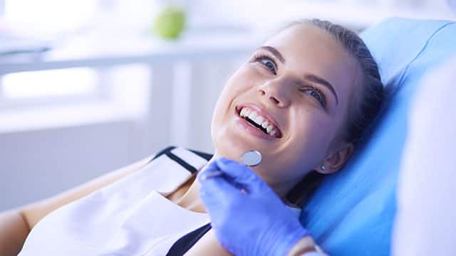 A young smiling woman in a dentist's chair.