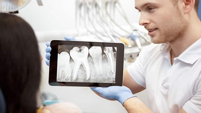 dentist showing his patient an x-ray of teeth on a  digital tablet 