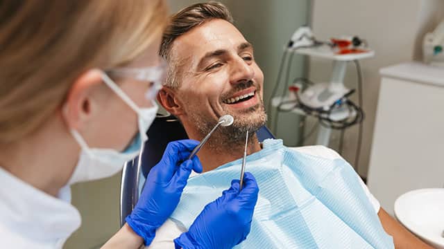 Happy young man sitting in a dental chair as a dentist stands over him with tools 