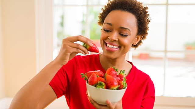 Young woman eating fresh strawberries from a bowl