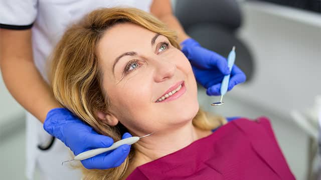 An older woman is at the dentist receiving a dental procedure