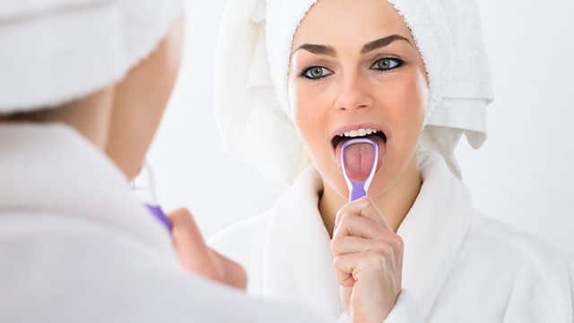 A woman cleaning her tongue in a bathroom