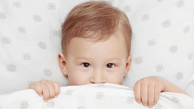 Child in a bed covering his lip with the blanket