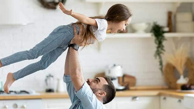 Happy smiling dad lifting his daughter in the air while in the kitchen.