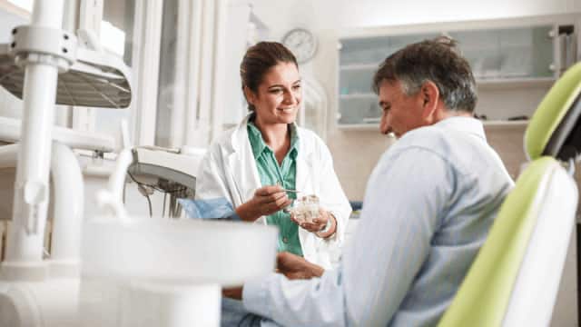 female dentist in dental office talking with senior male patient and preparing for treatment