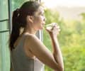 Asian woman drinking clean water in the morning next to the window with nature background
