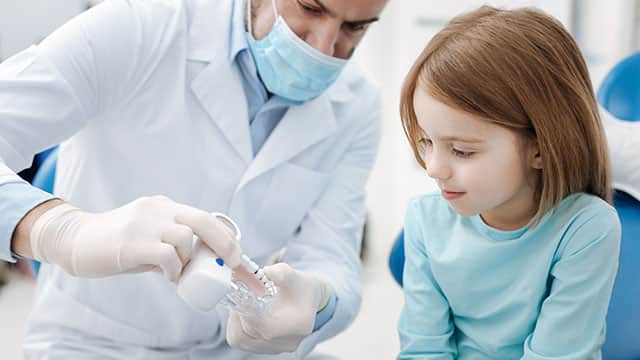 A male dentist explaining about teeth to a small girl in the dental office