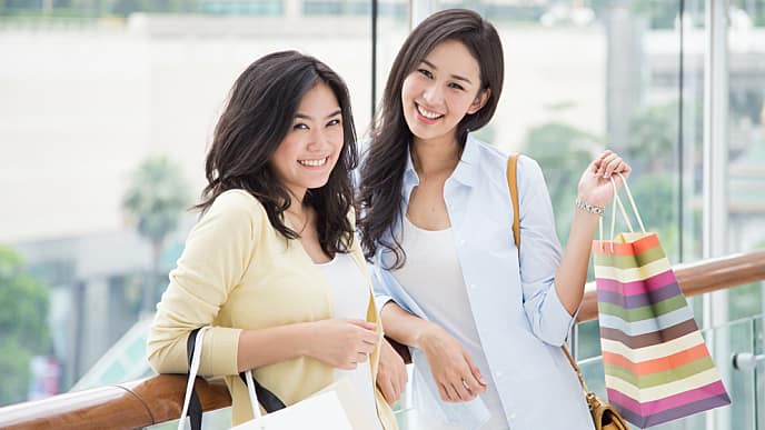 two woman smiling and holding shopping bags