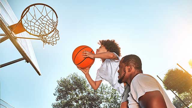 father is lifting up his kid to help him reach the basketball hoop