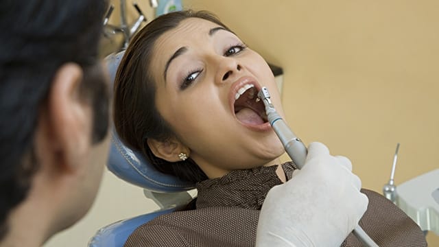 Dentist examining a woman's teeth for signs of injury.