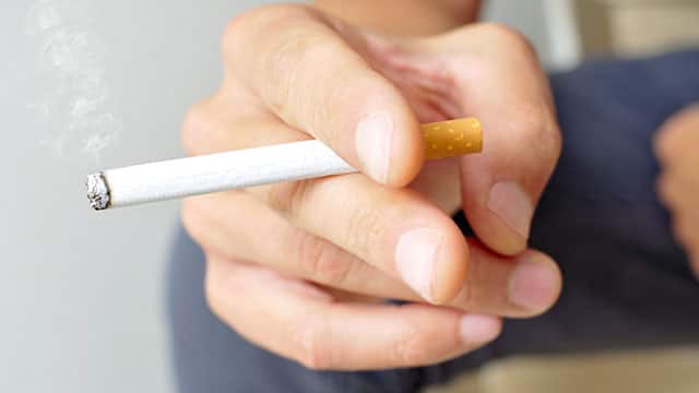 A close up of the man's hand holding a lit cigarette