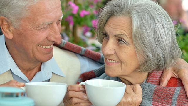 A senior couple sitting outside and smiling while drinking tea