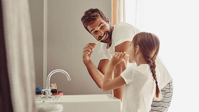 Father and daughter are brushing their teeth over the sink