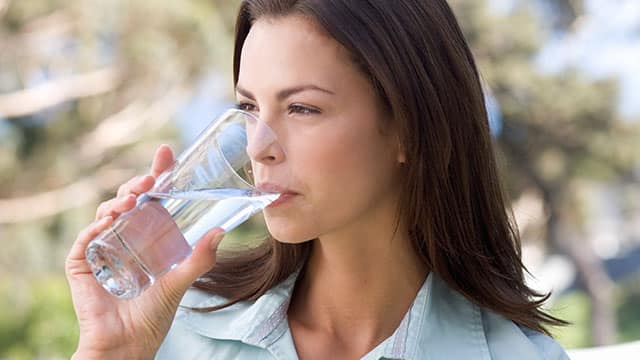 A young woman is drinking water from a glass outdoors