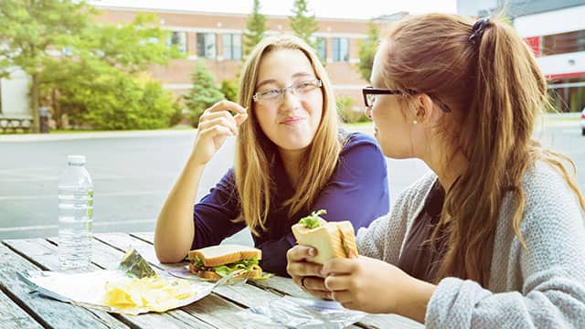 Two teen girls eating sandwiches outdoors