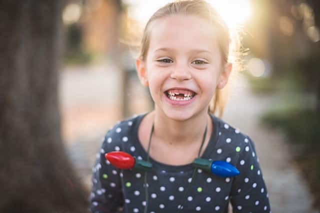 A small girl has a missing front tooth and smiling outdoors