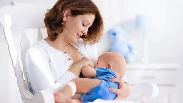 Happy young mother breastfeeding her baby at home