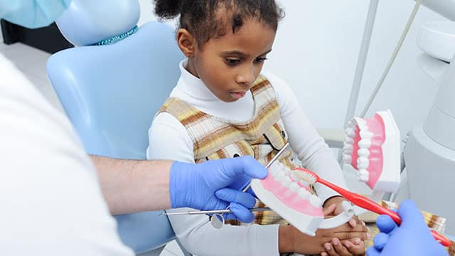 dentist teaching child how to brush her teeth using a mouth model 