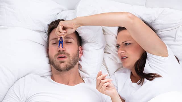 A woman Trying To Stop Man's Snoring With Clothespin