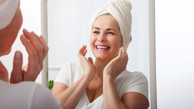 Smiling  woman looking at a mirror in a bathroom with hands near her jaw