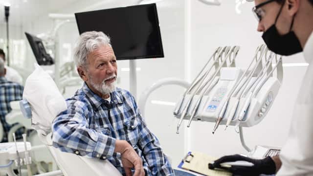 An senior man in a flannel shirt talking with his dentist