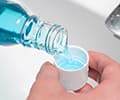 Close-up of a man's hands pouring mouthwash into a cap above the sink