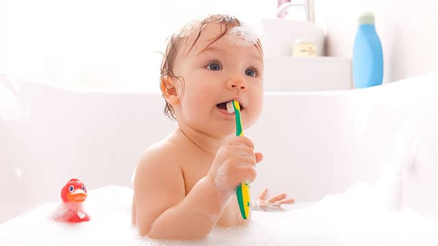 A baby is holding a tooth brush in the bathtub