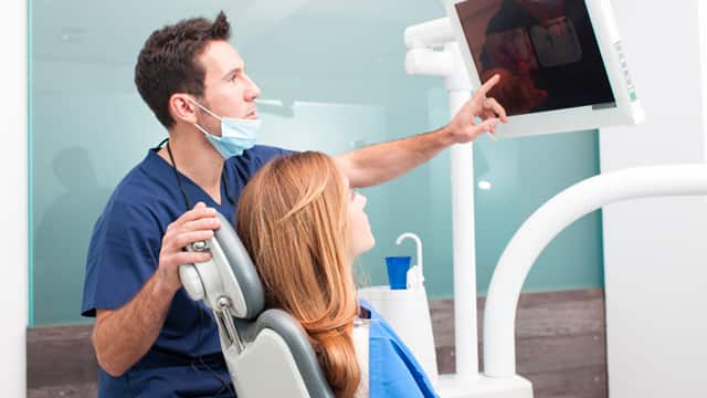 Dentist in scrubs with mask discussing x-ray results with patient in chair