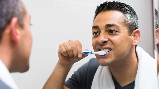 A man brushing his teeth in front of the bathroom mirror 