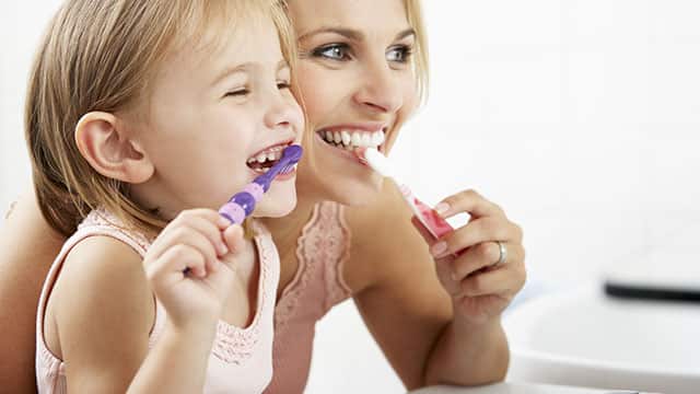 a mother and a daughter smiling brightly while brushing their teeth with Colgate toothbrush