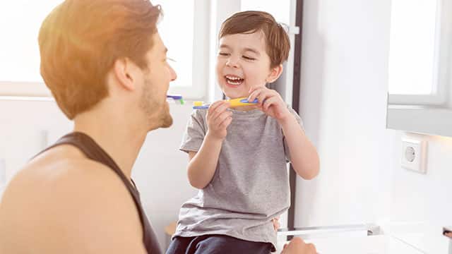Father and son laughing and brushing their teeth together in the bathroom