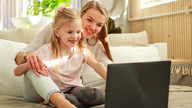 Happy family mother with daughter using computer laptop at home, modern lifestyle