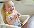 Little baby girl sitting in high chair and laughing indoors