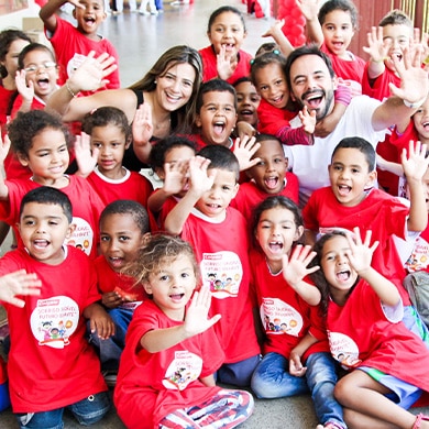 Group of children in red t-shirts waving enthusiastically with two adults.