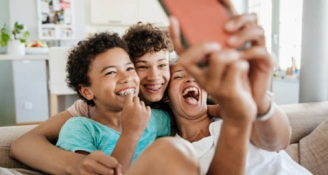 Niños sonriendo con brackets en una selfie familiar divertida en la sala.