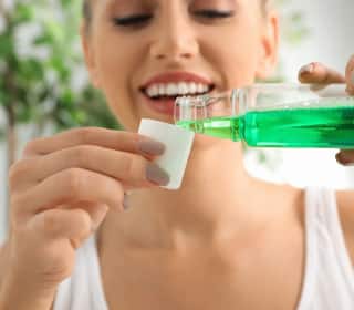 ภาพระยะใกล้ของผู้หญิงที่กำลังรินน้ำยาบ้วนปากจากขวดลงในฝา