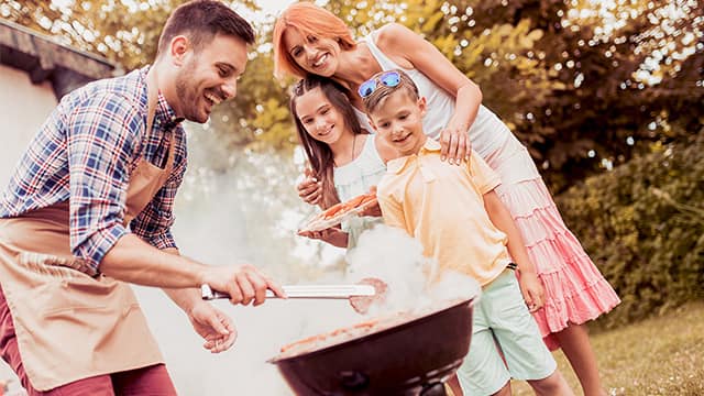 A happy family enjoys a backyard barbecue, with a man grilling and a woman and two children smiling